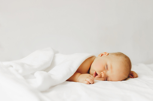 Beautiful baby sleeps on the bed in white sheets.